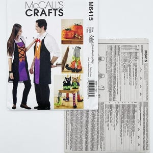May include: A McCall's Crafts M6415 sewing pattern envelope for adult aprons and decorative items. The front shows illustrations of aprons, pumpkin-shaped containers, a broom, and stuffed cat and owl figures with patterned fabric accents.