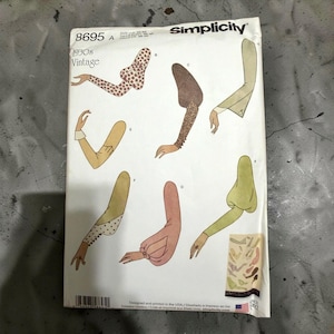 Pode incluir: Um envelope de molde de costura Simplicity, número 8695, com ilustrações de vários designs de mangas vintage dos anos 30. O envelope de papel branco exibe seis estilos de manga diferentes nas cores castanho, bege e verde, com texto.