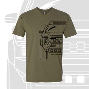 May include: A green t-shirt with a black outline of a truck's front end. The truck has a black grill and headlights.