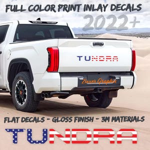 May include: A white pickup truck with a "TUNDRA" decal on the tailgate. The decal is in red, white, and blue with a stars and stripes pattern. The truck is parked on a sandy surface. The text "FULL COLOR PRINT INLAY DECALS 2022+ FLAT DECALS - GLOSS FINISH - 3M MATERIALS" is visible at the top and bottom of the image.