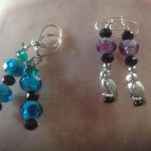 May include: A pair of dangle earrings with black, purple, and teal beads. One pair features a silver owl charm.