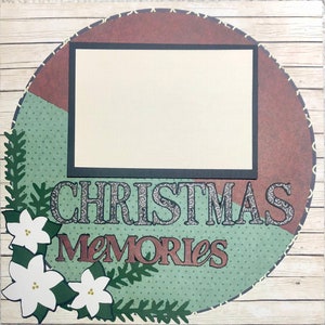 May include: A scrapbook page with a brown and green circular background. The background has a white rectangle in the center. The words "Christmas Memories" are printed in brown and black letters on the bottom of the page. There are white flowers with green leaves on the left side of the page.