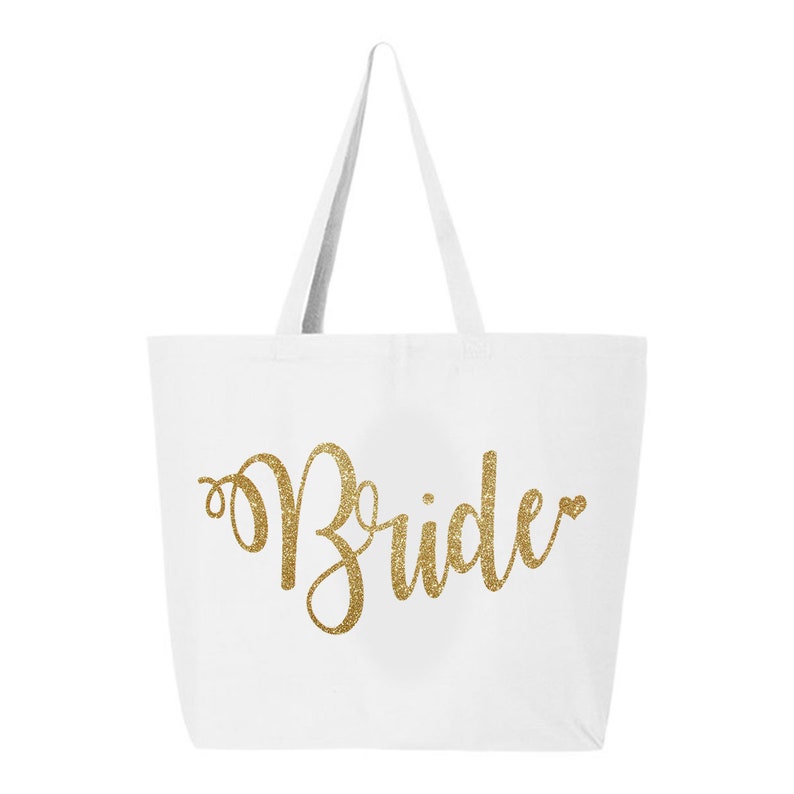 May include: White tote bag with gold glitter text that reads "Bride". The bag has two white handles and is made of a sturdy fabric. The design is simple and elegant, perfect for a wedding.