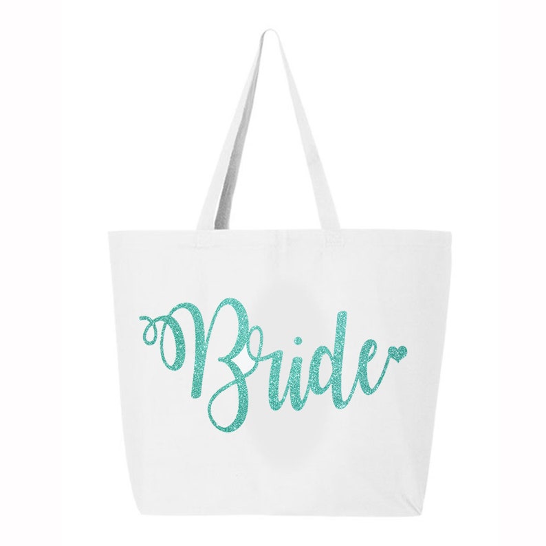 Puede incluir: Bolsa de lona blanca con un dise&ntilde;o de purpurina turquesa que dice "Bride" con un peque&ntilde;o coraz&oacute;n.