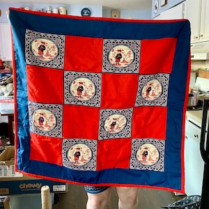 May include: A red and blue quilt with a repeating pattern of a person in a landscape. The quilt is made of squares and has a blue border.