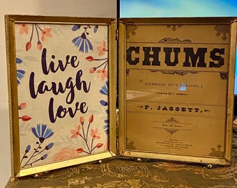 May include: Two gold-framed pictures, one with a floral pattern and the text "live laugh love", the other with the text "CHUMS (COMRADE TO CONRADES) BY P. JASSETT. Price 10 Cents."