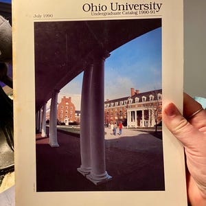May include: A white and red brick building with a white columned portico. The building is surrounded by trees and grass. The text "Ohio University Undergraduate Catalog 1990-91" is printed on the cover of the book. The text "July 1990" is printed on the cover of the book.