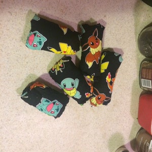 May include: Six small black fabric pouches with different Pokemon characters printed on them. The pouches are filled with something soft and are likely used as stress balls or toys.