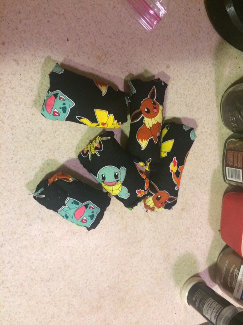 May include: Six small black fabric pouches with different Pokemon characters printed on them. The pouches are filled with something soft and are likely used as stress balls or toys.