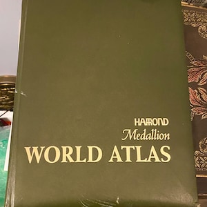 May include: A green hardcover book with the title "WORLD ATLAS" in gold lettering. The book is by Harrod Medallion.
