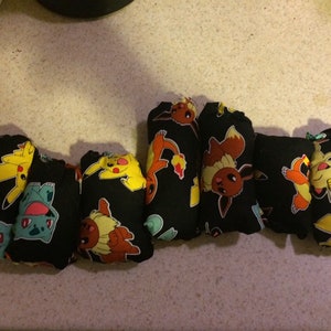 May include: A set of seven black cloth diapers with colorful Pokemon characters printed on them. The characters include Pikachu, Bulbasaur, Charmander, Squirtle, and Eevee.