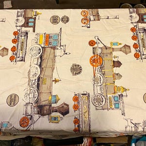 May include: Cream-colored fabric with a repeating pattern of vintage train illustrations in shades of brown, orange, yellow, and blue. The design includes train wheels, cabins, and the word "ERIE".