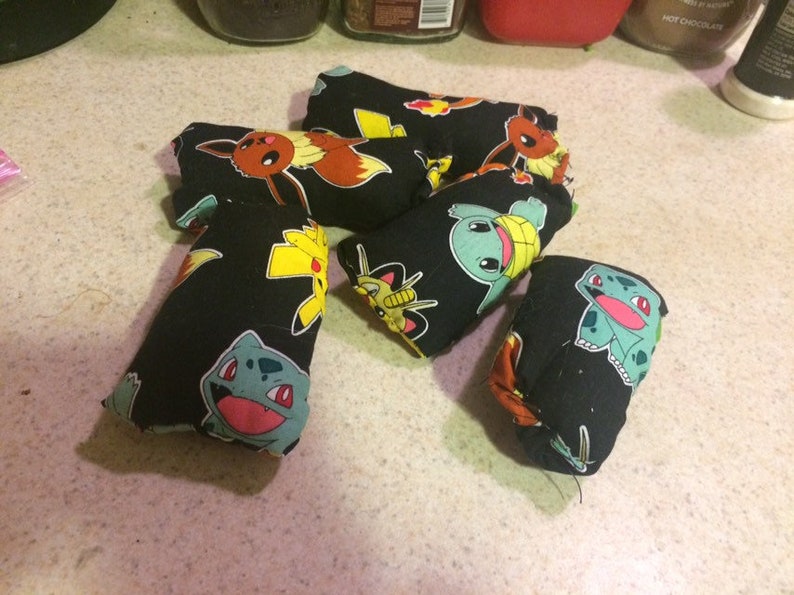 May include: Six black fabric pouches with different Pokemon characters printed on them. The pouches are filled with something soft and are likely used as stress balls or fidget toys.