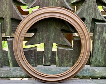 May include: A circular picture frame with a smooth, light brown wooden finish. The frame features a multi-tiered, stepped profile that creates depth and dimension. The design is simple and clean, focusing on the natural wood grain and circular shape.