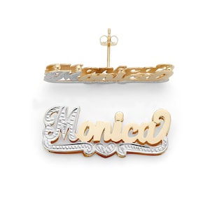 Op de afbeelding: Gouden en zilveren naamplaatje oorbel met de naam "Monica" in een cursief schrift. De oorbel is ontworpen met een hartvorm aan het einde van de naam.