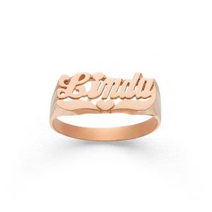 May include: A rose gold ring with the name "Linda" engraved in a cursive font. The ring has a small heart detail in the centre.