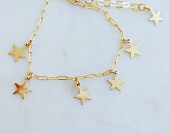 May include: A gold chain bracelet with five dangling star charms. The bracelet is made of a delicate chain and the stars are a simple, classic design.