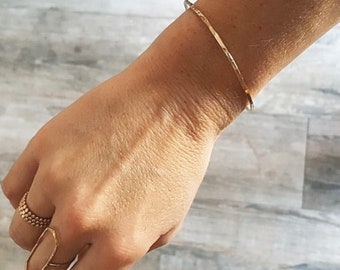 May include: A gold hammered bangle bracelet on a person's wrist.