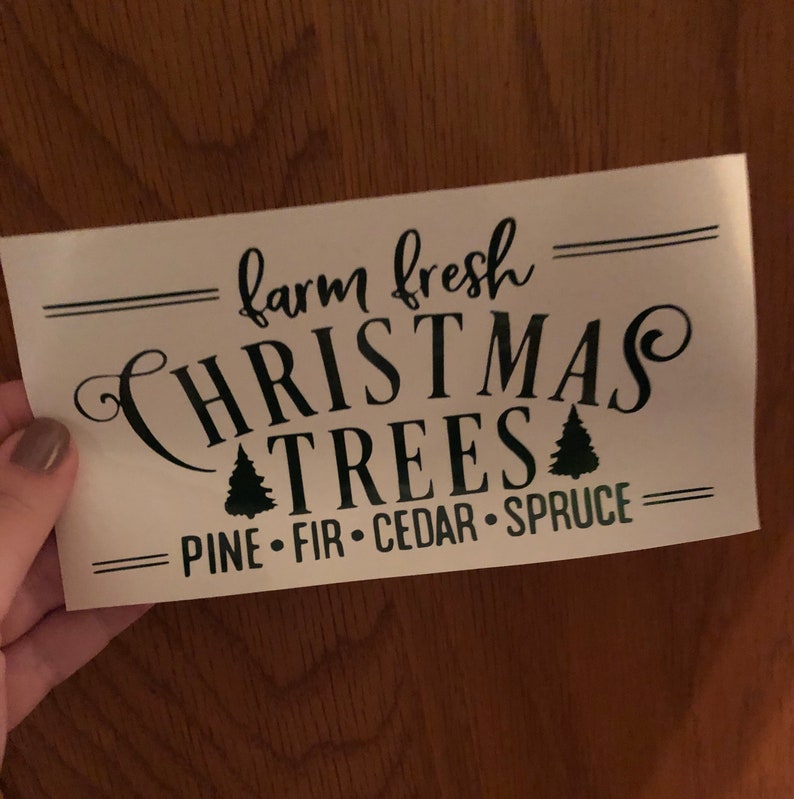 Pu&ograve; includere: Un cartello bianco con testo nero che recita "farm fresh CHRISTMAS TREES PINE - FIR - CEDAR - SPRUCE". Il cartello ha due piccoli alberi di Natale neri.