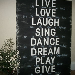 May include: Black wooden sign with white text that reads "Live like heaven is on Earth, Love like you have never been hurt, Laugh like no one is listening, Sing as if no one can hear, Dance as if no one is watching, Dream like there are no impossibilities, Play like there are no winners, Give like you have plenty."