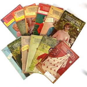 May include: A collection of vintage "Workbasket" magazines, featuring covers with images of crochet projects, children, and women. The magazines have a red and white color scheme with the title in bold letters. The magazines are fanned out on a white surface.