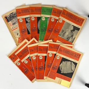 May include: A collection of vintage "The Workbasket" magazines. The covers are primarily orange with black and white illustrations and text. Some covers feature images of women and knitting patterns. The price is 15 cents.