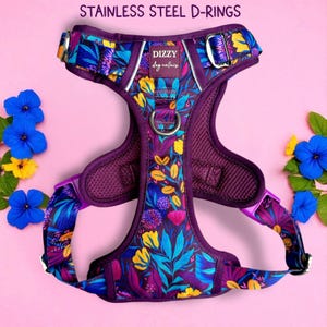 Könnte beinhalten: Ein lila Hundegeschirr mit einem Blumenmuster mit gelben, blauen und lila Blumen und Blättern. Das Geschirr hat D-Ringe aus Edelstahl und den Text "DIZZY dog collars". Der Hintergrund ist rosa.