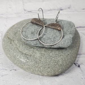 May include: A pair of silver hoop earrings with a brown leather accent on each hoop.