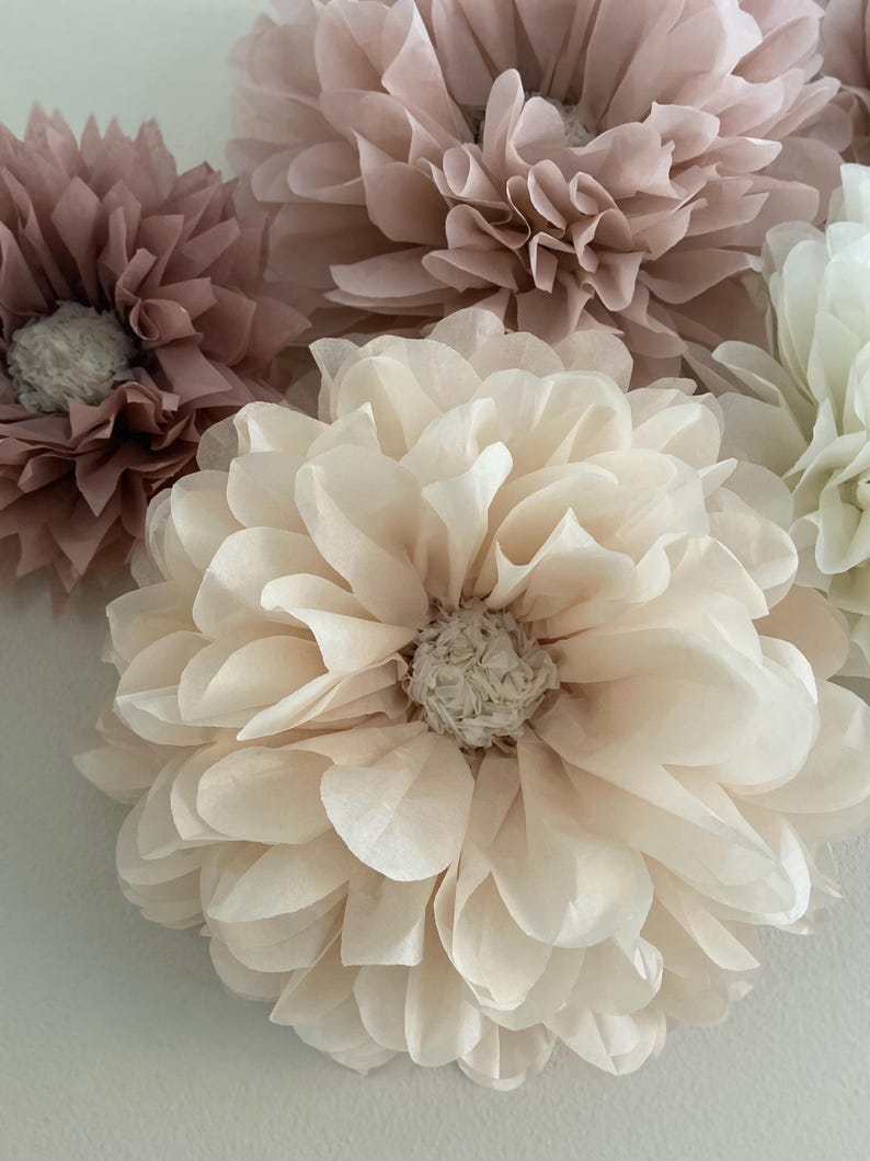 May include: A set of four tissue paper flowers in shades of pink and cream. The flowers are layered and ruffled, creating a delicate and romantic look.