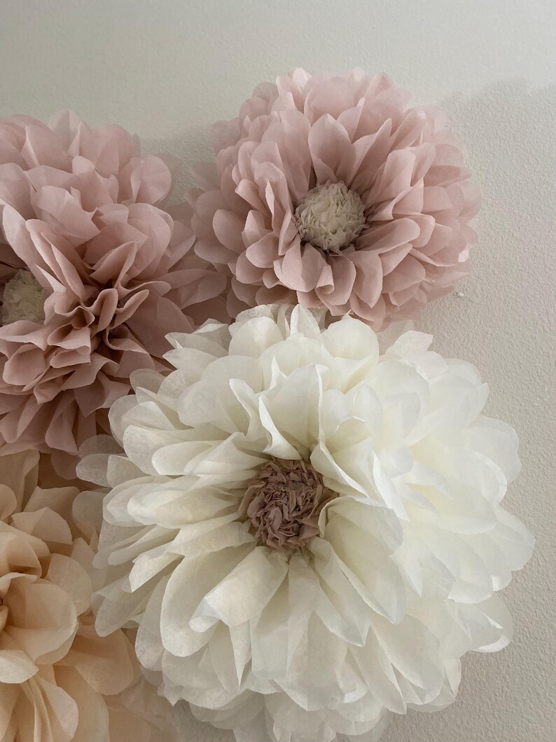 May include: Four large paper flowers in shades of pink and white. The flowers are made of tissue paper and have a layered, fluffy texture.
