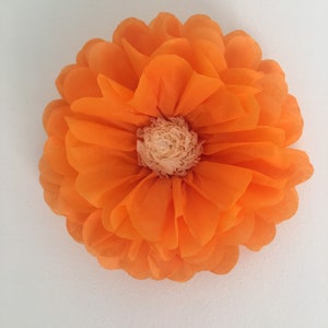 Puede incluir: Una gran flor de papel naranja con m&uacute;ltiples capas de p&eacute;talos y un centro beige claro. La flor es redonda y parece estar hecha de papel fino y transl&uacute;cido. Los p&eacute;talos son de color naranja vibrante.