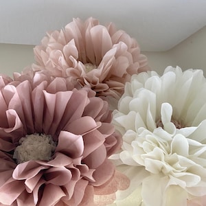 May include: Three large tissue paper pom-poms in shades of blush pink and white. The pom-poms are a popular decoration for parties and events.