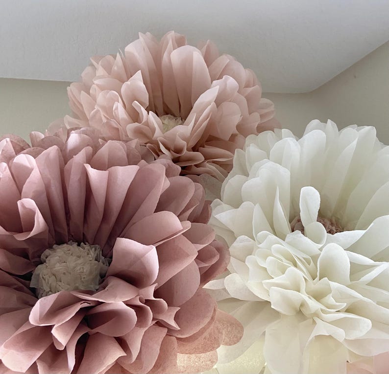 May include: Three large tissue paper pom-poms in shades of blush pink and white. The pom-poms are a popular decoration for parties and events.
