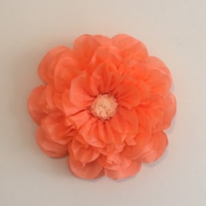 Puede incluir: Una gran flor de papel de color coral con m&uacute;ltiples capas de p&eacute;talos. La flor tiene un aspecto texturizado y un centro beige claro. Los p&eacute;talos est&aacute;n dispuestos en un patr&oacute;n circular, creando un efecto de floraci&oacute;n completo. Adecuado para proyectos de manualidades.