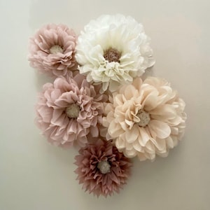 May include: A set of six tissue paper flowers in shades of pink and cream. The flowers are arranged in a cluster and have a delicate, ruffled texture.