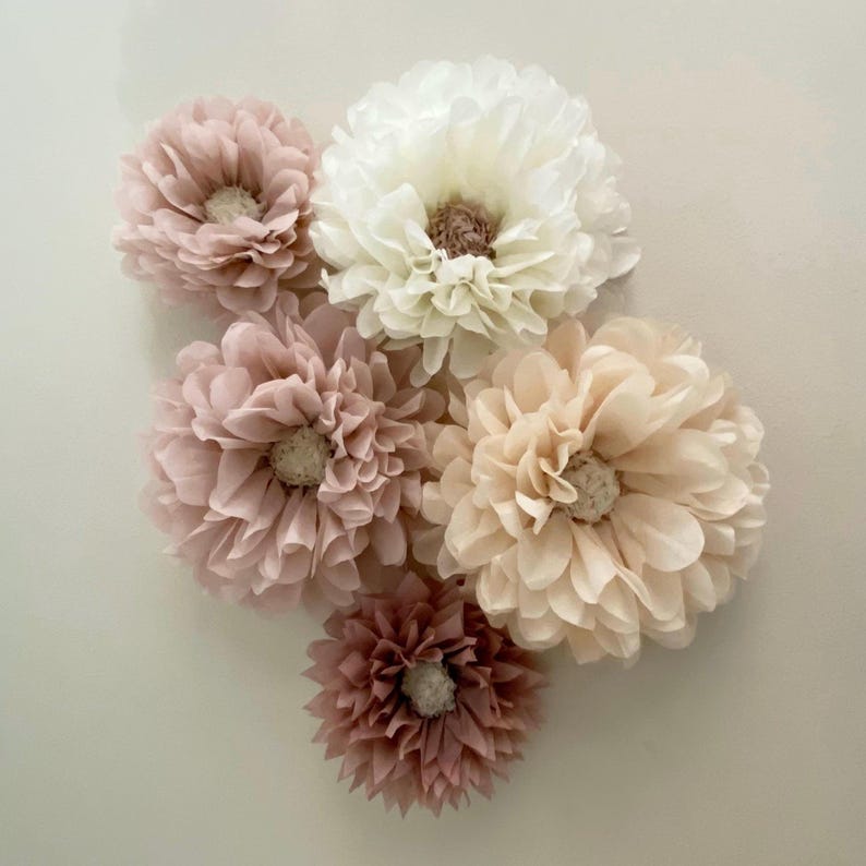 May include: A set of six tissue paper flowers in shades of pink and cream. The flowers are arranged in a cluster and have a delicate, ruffled texture.