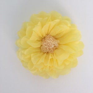 Puede incluir: Una flor de papel amarilla, grande y redonda, con m&uacute;ltiples capas de p&eacute;talos. El centro de la flor es de color beige claro. La flor probablemente se utiliza para decoraci&oacute;n o manualidades.
