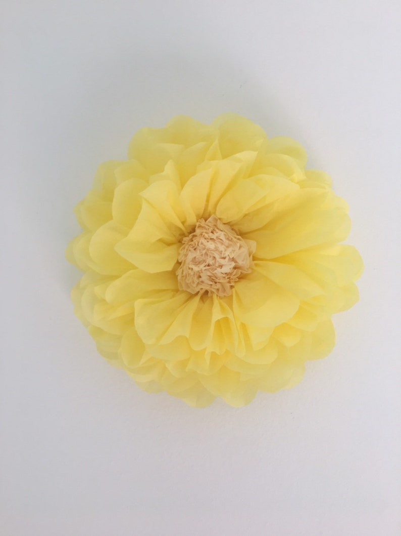 Puede incluir: Una flor de papel amarilla, grande y redonda, con m&uacute;ltiples capas de p&eacute;talos. El centro de la flor es de color beige claro. La flor probablemente se utiliza para decoraci&oacute;n o manualidades.