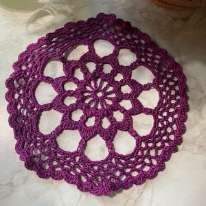 May include: A purple crocheted doily with a delicate floral design.