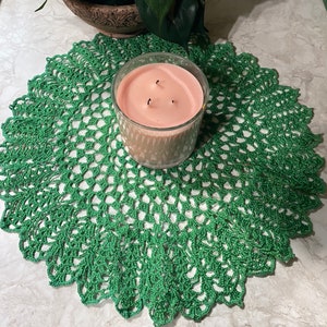 May include: A green crocheted doily with a pink candle in the centre. The candle has three wicks.
