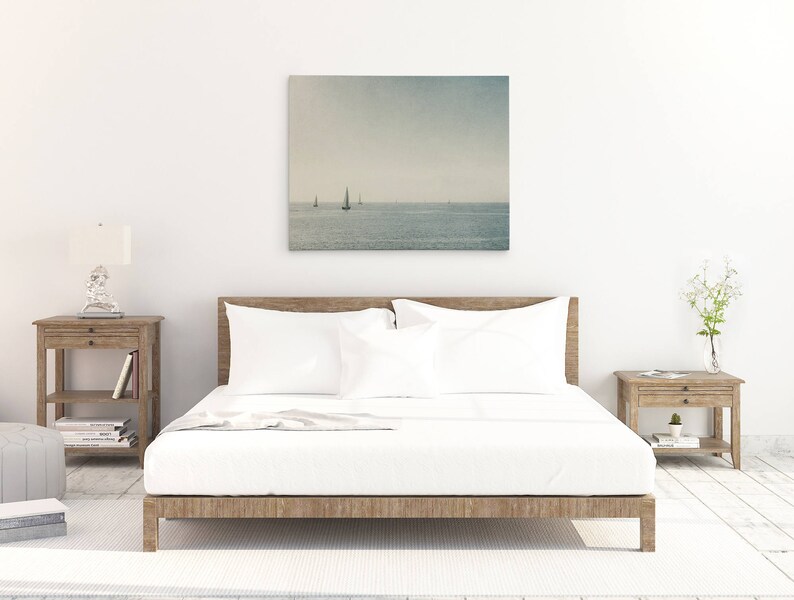 May include: A white bed with a wooden frame and white bedding. A framed photograph of a seascape with sailboats hangs above the bed. Two wooden nightstands with drawers are on either side of the bed.