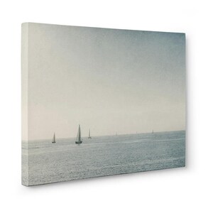 May include: A photograph of a seascape with a hazy sky and several sailboats in the distance. The water is a light blue color and the sky is a light gray color.