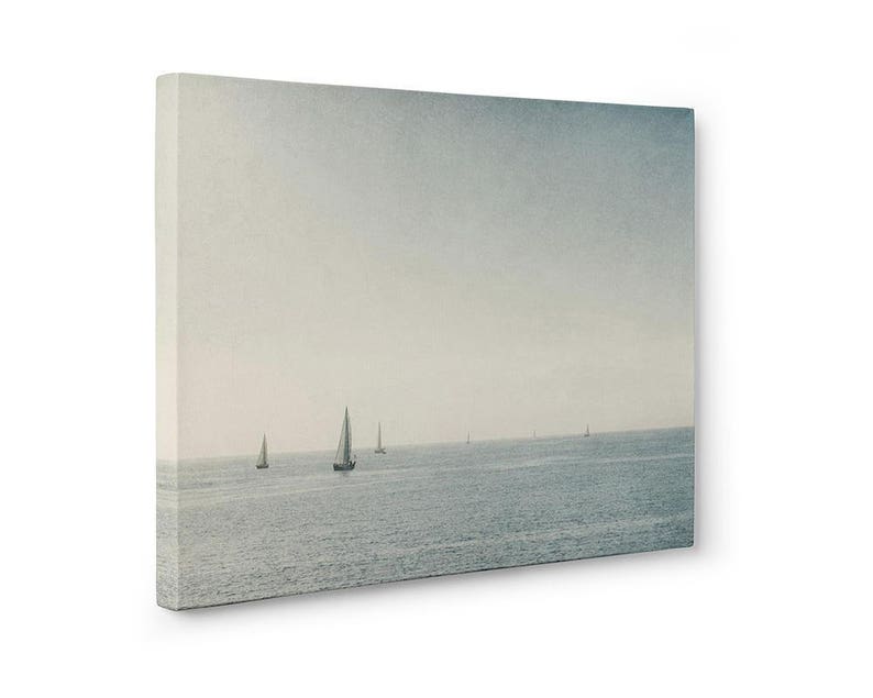 May include: A photograph of a seascape with a hazy sky and several sailboats in the distance. The water is a light blue color and the sky is a light gray color.