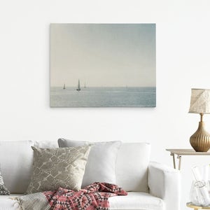 May include: A photograph of a seascape with several sailboats in the distance. The sky is a light blue and the water is a calm, light blue. The image is taken from a distance, so the sailboats are small and appear to be far away.