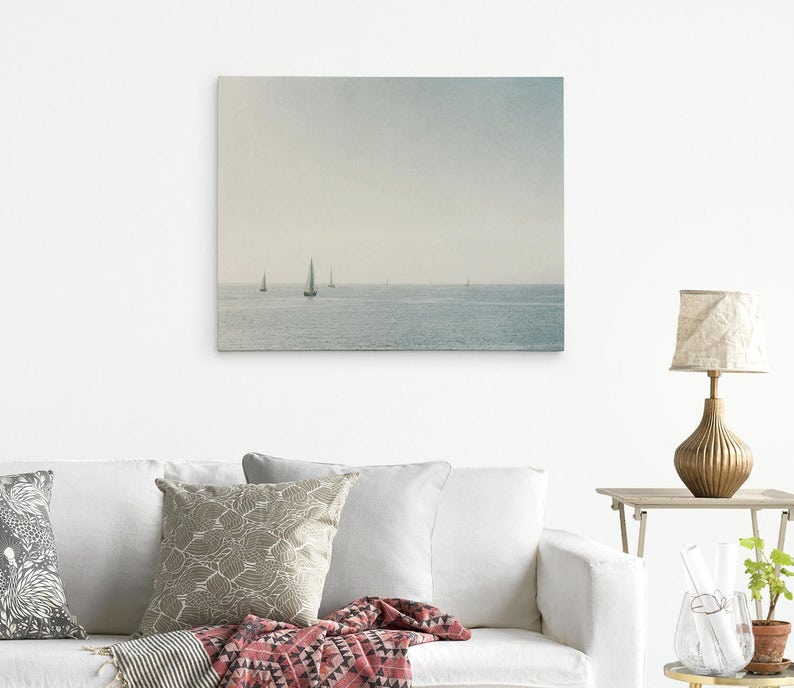 May include: A photograph of a seascape with several sailboats in the distance. The sky is a light blue and the water is a calm, light blue. The image is taken from a distance, so the sailboats are small and appear to be far away.