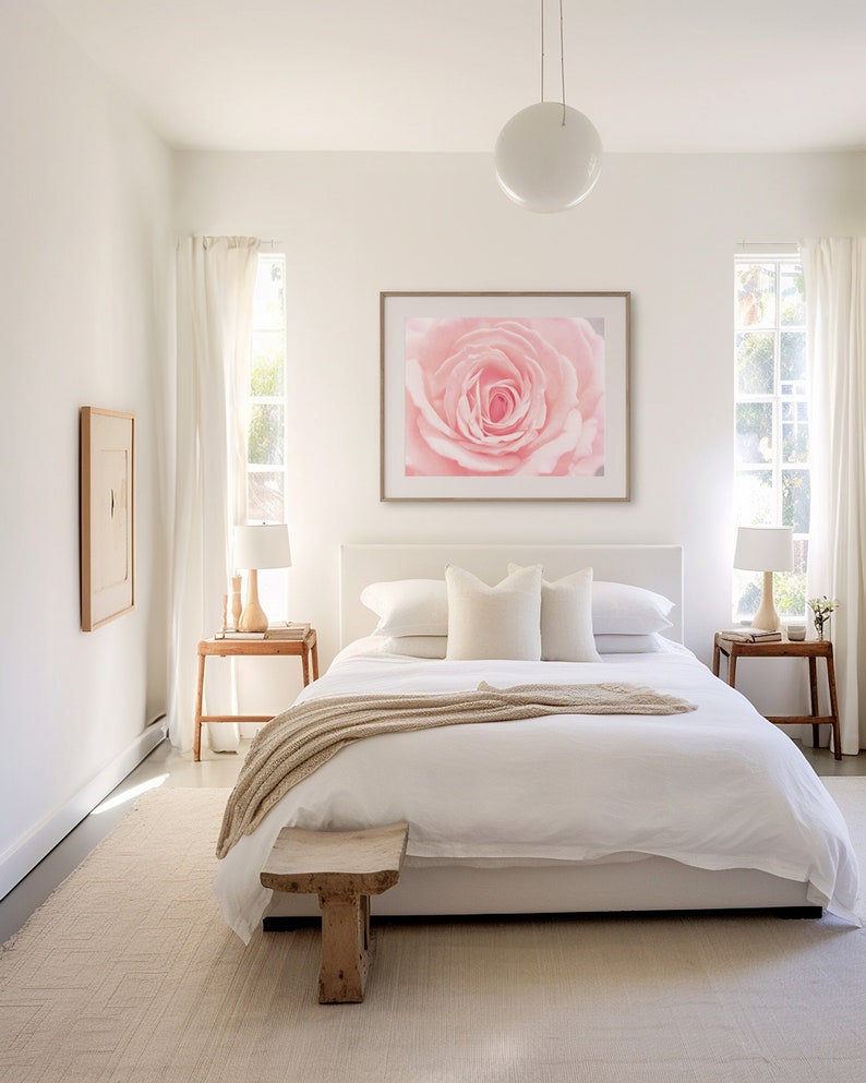 Pu&ograve; includere: Un letto bianco con un copripiumino bianco e una coperta beige. Ci sono due cuscini bianchi e un cuscino beige sul letto. Una stampa incorniciata di una rosa rosa &egrave; appesa al muro sopra il letto.