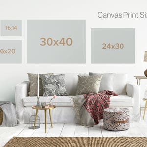 May include: A white couch with pillows and a throw blanket in a living room setting. The wall behind the couch has a sign that reads "Canvas Print Sizes" with four different sizes listed: 11x14, 16x20, 30x40, and 24x30.