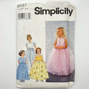 May include: A Simplicity sewing pattern envelope featuring illustrations of girls' dresses. The dresses include a blue floral dress, a yellow floral dress, and a pink tulle dress with floral accents. The envelope is white with the Simplicity logo.