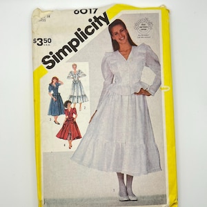 May include: A vintage Simplicity sewing pattern envelope. The envelope is yellow and white, featuring illustrations of dresses and the text "Simplicity" in large black letters. The price is $3.50.