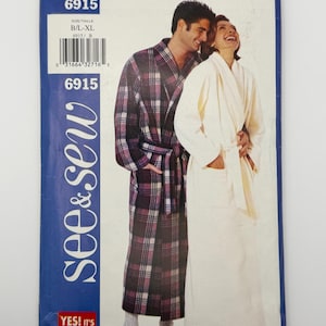 May include: A See & Sew sewing pattern envelope 6915 featuring two full-length robes. One robe is a dark purple, black, and white plaid pattern with a tie belt. The second robe is solid cream with a shawl collar and a matching tie belt.